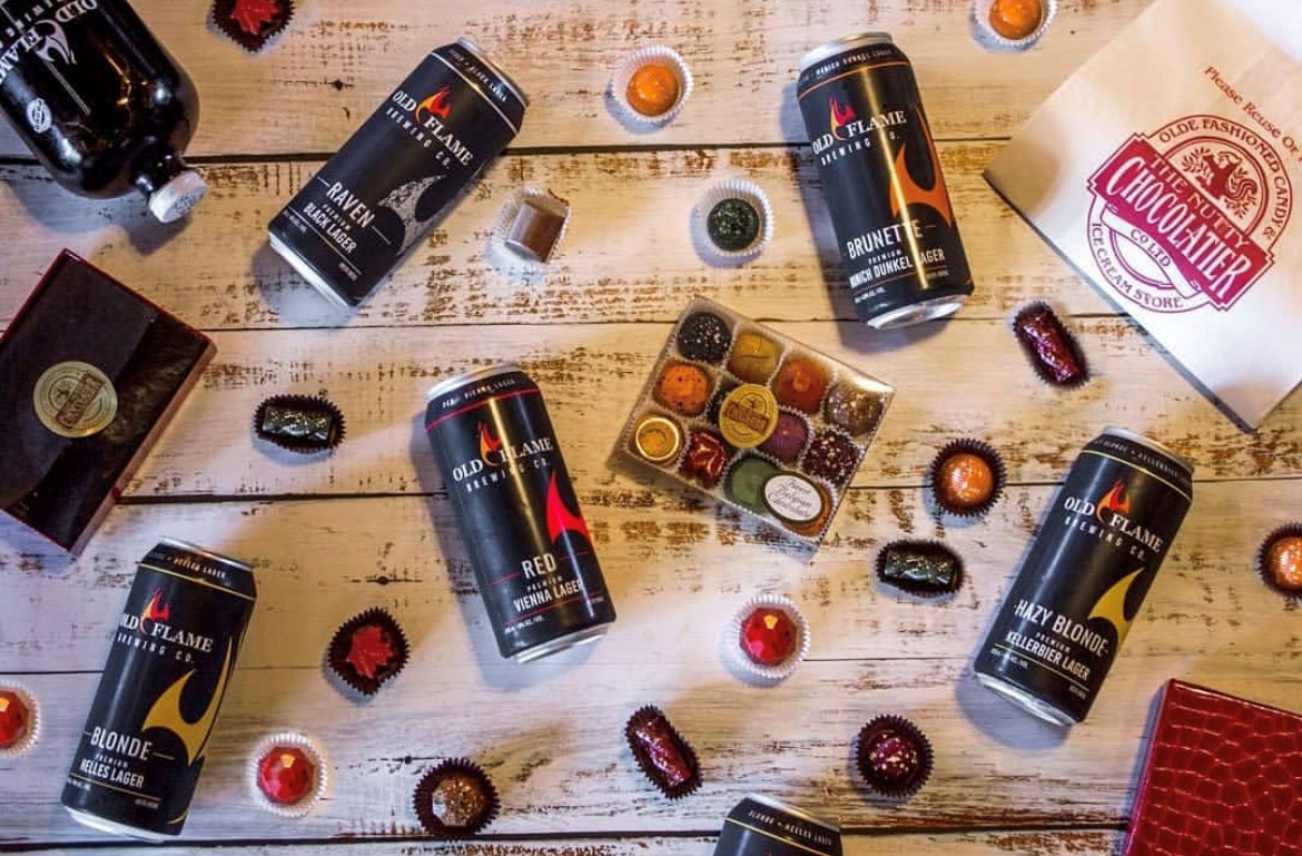 Old Flame Brewery beer and Nutty Chocolatier chocolates Old flame beer cans on a wooden table surrounded by Nutty Chocolatier chocolates