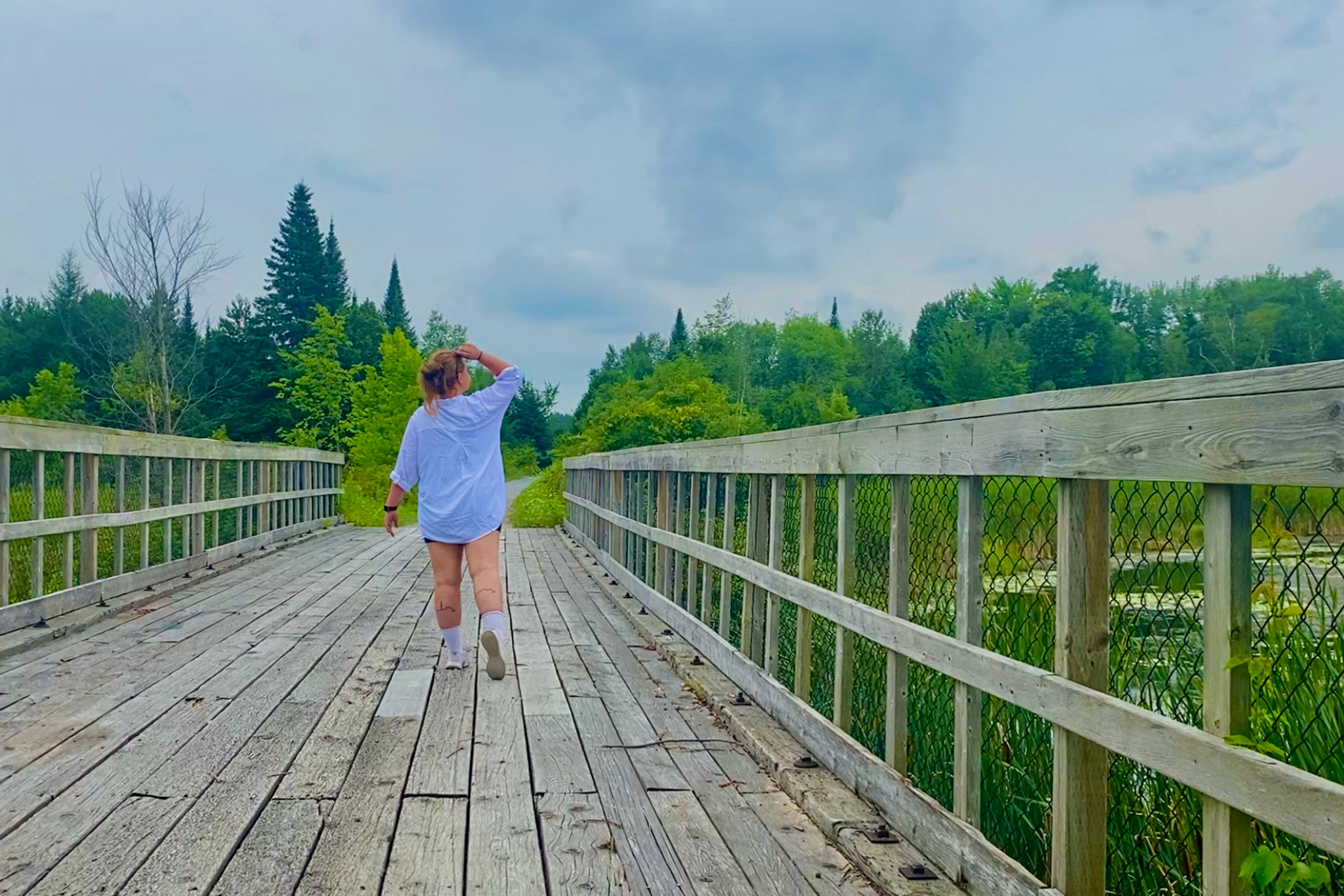 Image of a person walking away from the camera, down a boardwalk through a wetland